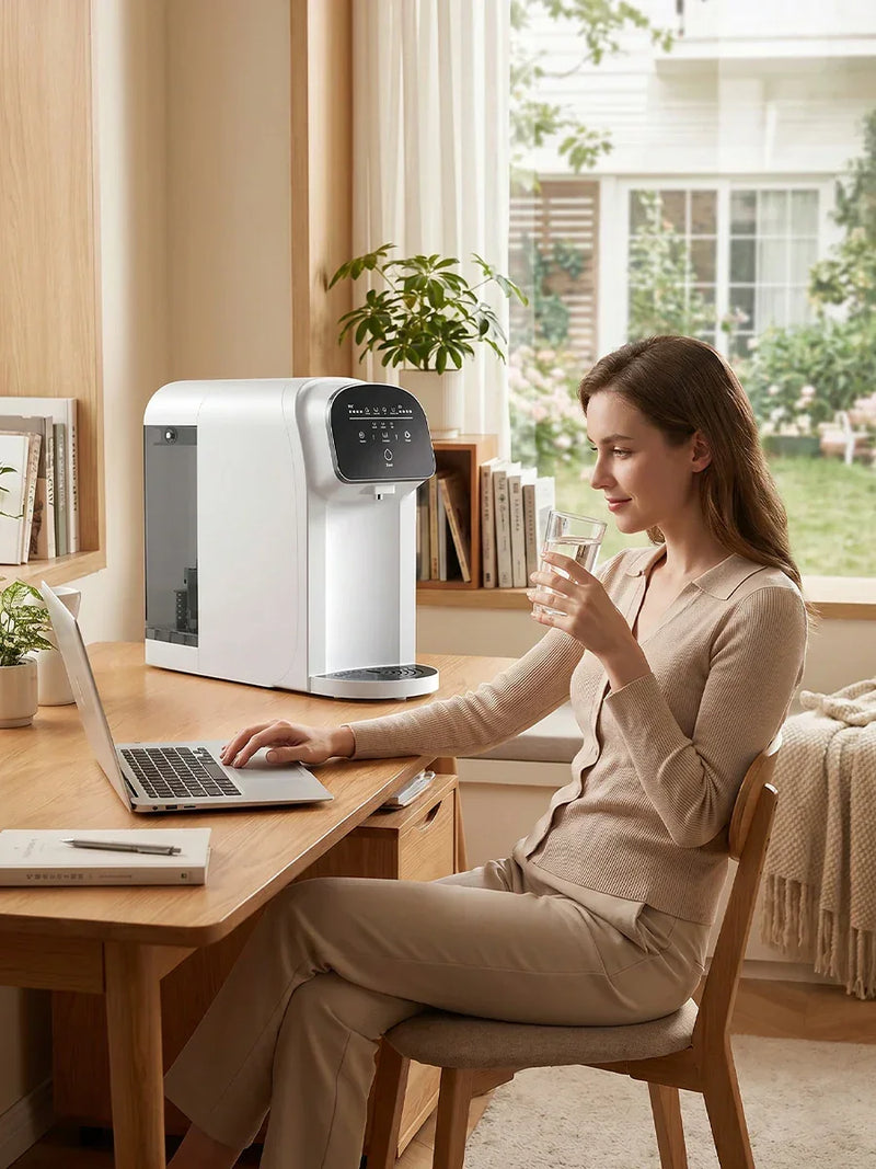 Woman drinking purified water from countertop reverse osmosis filter while working at desk